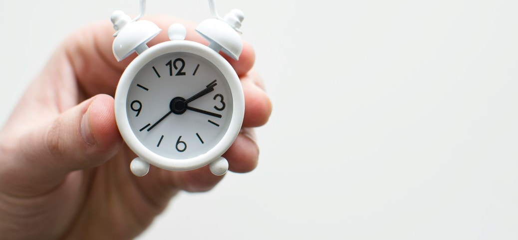 Eine Hand hält einen kleinen weißen Wecker, der 3:10 anzeigt – Symbol für die Schlafenszeit.