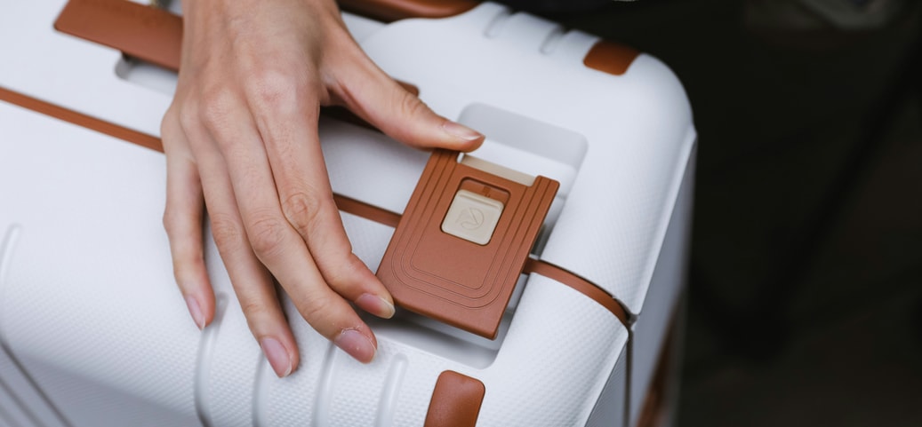 Person legt beim Koffer packen ihre Hand auf ein modernes Schloss eines weißen Hartschalenkoffers mit braunen Akzenten.