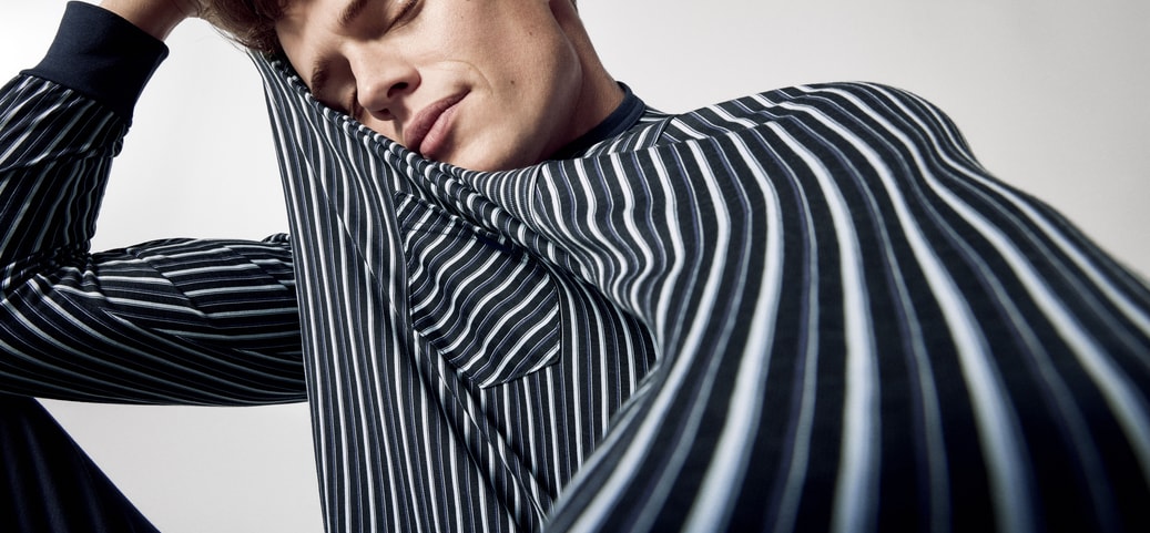 A man with his eyes closed, bending his right arm to support his head and wearing CALIDA nightwear.