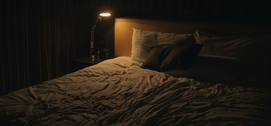 Camera da letto buia con illuminazione fioca da una lampada da comodino, letto disordinato: simboleggia l'atmosfera opprimente di un incubo.
