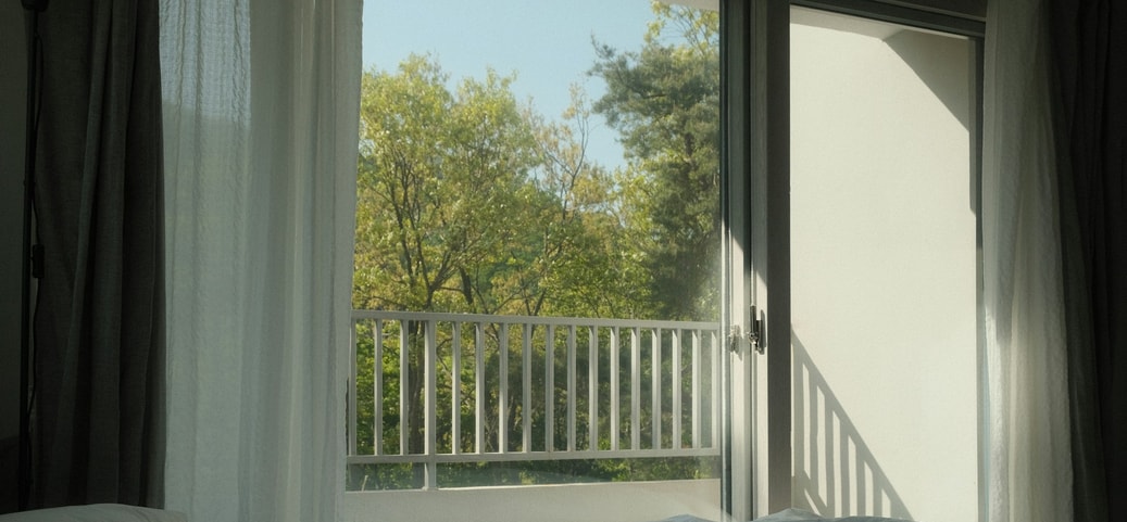Fenêtre ouverte avec vue sur la verdure – symbole d’aérer avant de dormir pour un meilleur climat intérieur.