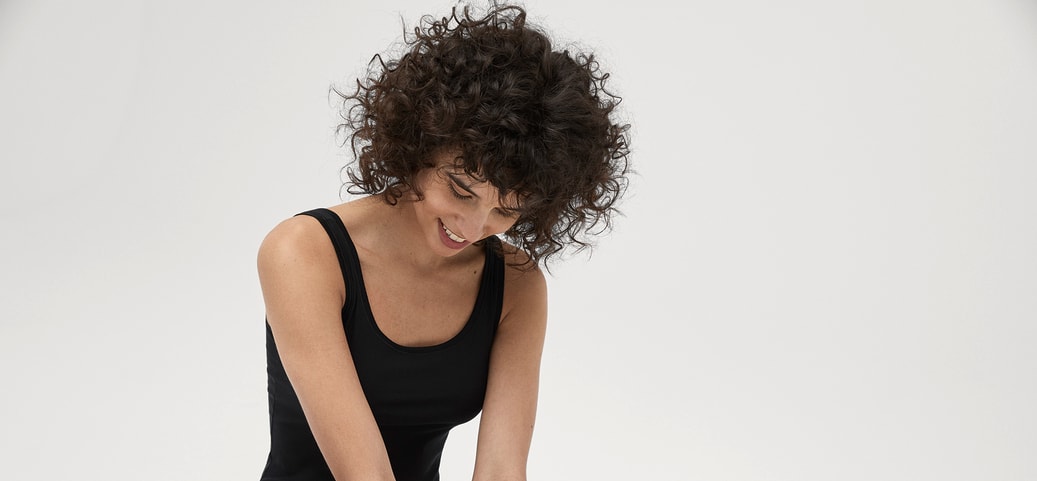 Autumn type colours: Woman with curly hair in black CALIDA Iconics bodysuit against white background