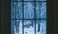 Verschneiter Wald mit altem roten Wagen, durch ein Fenster betrachtet – ruhige Winterstimmung als Symbol für den Winterblues
