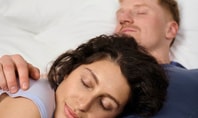 Deux personnes dormant étroitement blotties ensemble sur un lit blanc – une position typique de sommeil pour un couple.