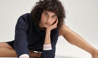 Person sitting relaxed on a white surface wearing a navy long‑sleeve top with striped cuffs – minimalist, calm fashion shot
