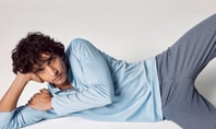Man lying on his side on a light surface, wearing a light blue long‑sleeve shirt and patterned blue trousers