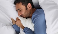 Schlafender Mann in blauer Nachtwäsche in weissem Bett; Symbolbild für erholsamen Schlaf und ein starkes Immunsystem