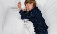 Personne qui dort dans des vêtements de nuit à motifs étoilés bleu foncé sur un lit blanc