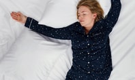 Sleeping person in dark blue star‑patterned sleepwear on a white bed; symbolic image for the topic of feeling cold and sweating at the same time during the night