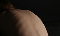 Gros plan d'un dos humain dans une lumière tamisée ; image symbolique pour le sujet de la meilleure position de sommeil pour les douleurs aiguës du bas du dos