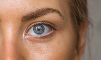Close‑up of a woman’s eye with a blue‑grey iris; fine skin details visible, the woman is wearing contact lenses