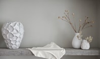 Scène de décoration minimaliste avec des vases blancs et du tissu sur une étagère grise ; une Culotte Midi Seamless CALIDA de la série Natural Skin placée au premier plan