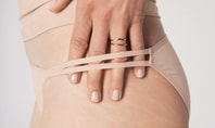 Une femme porte un slip tanga CALIDA ECO SENSE et tient 4 doigts à travers le tanga au niveau des hanches