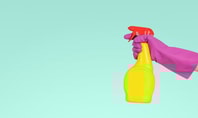 Eine Hand mit einem pinken Handschuh hält eine gelbe Sprühflasche mit rotem Deckel vor einem türkisfarbenen Hintergrund.