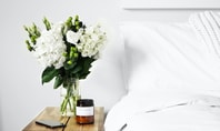 Bed with white bed linen and bedside table. There is a mobile phone and a candle on the bedside table.