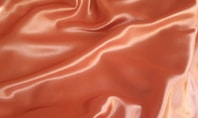 Nahaufnahme eines orangefarbenen, glänzenden Polyesterstoffs mit weichen Falten.