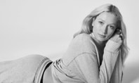 Woman lying on the floor and supporting herself with her elbows. The picture is black and white. She is wearing a gray sweatshirt.