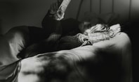 Person lies relaxed in a bed and reads a book in the dim light to calm down and fall asleep better.
