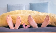 Eltern und Baby beim Co-Sleeping, ihre Füße schauen gemeinsam unter der Bettdecke hervor.