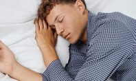 A man lies awake in bed with his eyes closed, answering the question: Why can't I sleep even though I'm tired?