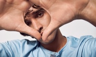 Close-up of a young man in a blue shirt holding his hands in front of his face in the shape of a heart. Symbolises concentration and mindfulness, in keeping with the theme of mindfulness exercises.