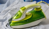 A green Philips iron on a garment - tips and techniques for correct ironing made easy.