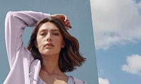 Frau mit blauem Hintergrund trägt Lavendel-Farbige Kleidung. Karierter Bustier und Loungewear-Jacke von CALIDA aus den Serien Elastic Trend und Lounge Tulip.
