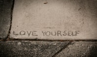 In den Beton eingravierter Schriftzug 'LOVE YOURSELF' – Selbstliebe lernen und sich selbst wertschätzen.