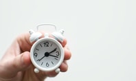 Eine Hand hält einen kleinen weißen Wecker, der 3:10 anzeigt – Symbol für die Schlafenszeit.