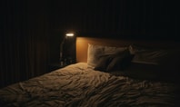 Camera da letto buia con illuminazione fioca da una lampada da comodino, letto disordinato: simboleggia l'atmosfera opprimente di un incubo.