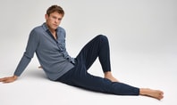 Man in comfortable sleepwear made from breathable fabric sitting relaxed on the floor against a neutral background.