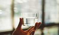 Main tenant un verre d’eau à la lumière – symbole de boire avant de dormir pour un meilleur repos.