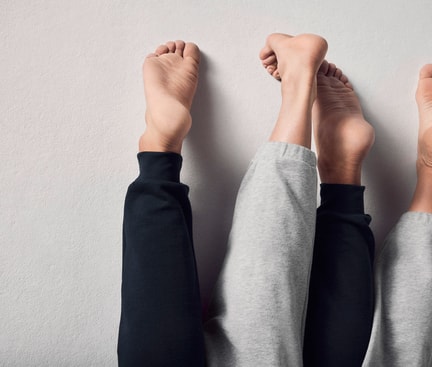 Deux paires de pieds nus en pantalon de jogging sont posées côte à côte sur une surface claire.