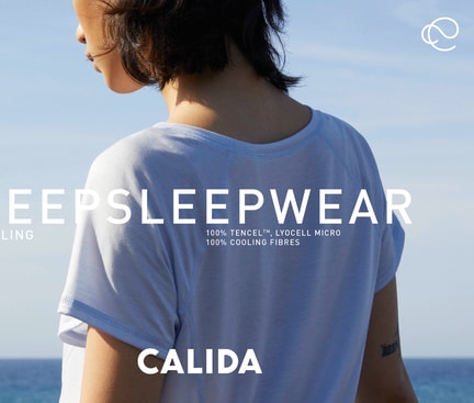 Rear view of a person wearing a light blue DEEPSLEEPWEAR short‑sleeve shirt by the sea, with overlaid text highlighting cooling TENCEL Lyocell sleepwear for menopause.