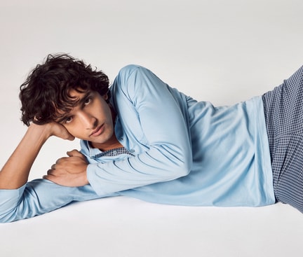 Man lying on his side on a light surface, wearing a light blue long‑sleeve shirt and patterned blue trousers