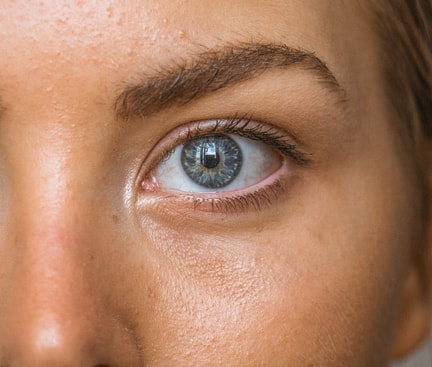 Close‑up of a woman’s eye with a blue‑grey iris; fine skin details visible, the woman is wearing contact lenses