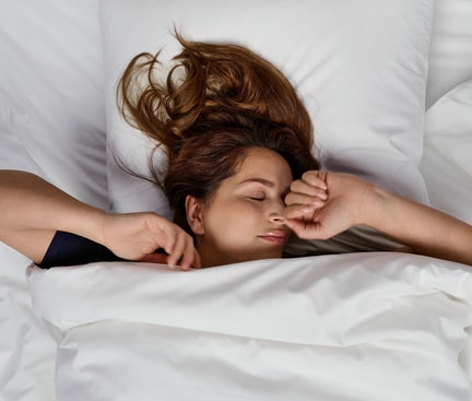 Person lying under a white duvet on a white pillow, resting peacefully; calm sleep scene used in the context of magnesium before bedtime