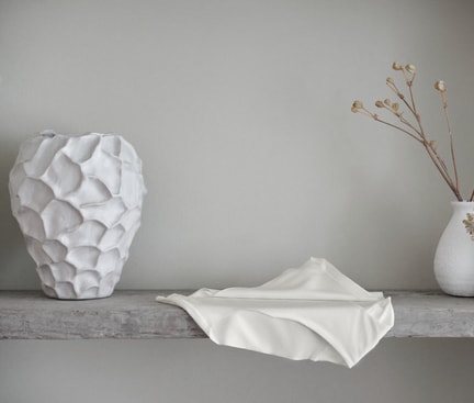 Minimalist decor scene with white vases and fabric on a grey shelf; a CALIDA Seamless Midi Slip from the Natural Skin series placed in the foreground