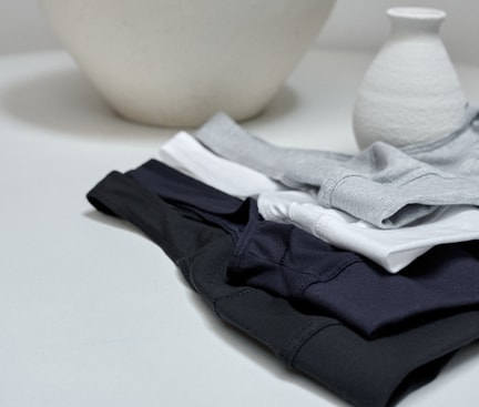 Several CALIDA bustiers from the Elastic collection in various colours, folded on a light-coloured table in front of decorative vases.