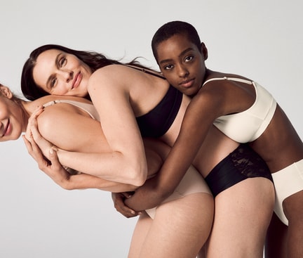  Auf dem Bild sind drei Frauen zu sehen, die sich von hinten umarmen. Sie stehen vor einem weißen Hintergrund, der ihre zärtliche Umarmung hervorhebt. Die Frauen tragen Unterwäsche von CALIDA, deren zarte Stoffe ihre Konturen sanft umspielen. Die Atmosphäre strahlt Verbundenheit und Zuneigung aus, während die Frauen sich liebevoll aneinander schmiegen.