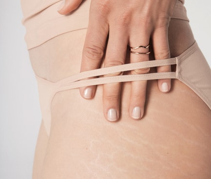 Frau trägt einen CALIDA ECO SENSE Tanga-Slip und hält 4 Finger durch den Tanga an der Hüfte