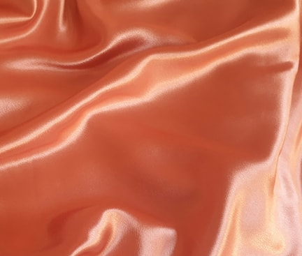 Nahaufnahme eines orangefarbenen, glänzenden Polyesterstoffs mit weichen Falten.