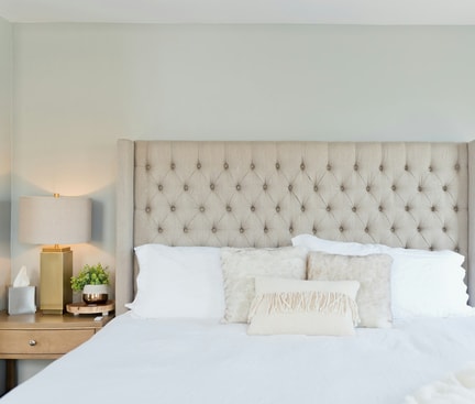 Helles Schlafzimmer mit beigem, gepolstertem Kopfteil, zwei Nachttischen, goldenen Lampen und weißer Bettwäsche – Symbol für trockene Luft im Schlafzimmer.