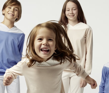 Vier Kinder in altersgerechten Schlafanzügen, die fröhlich in die Kamera schauen, symbolisieren den Schlafbedarf bei Kindern und die Bedeutung von bequemer Nachtkleidung für erholsamen Schlaf