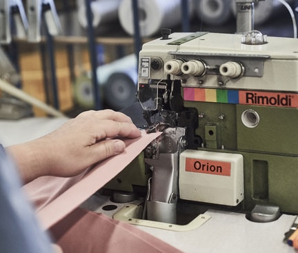 Eine Person repariert kleine Löcher in Kleidung mit einer professionellen Nähmaschine in einer Werkstatt.