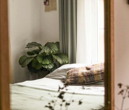 Ein Bett mit einer grünen Decke. Weisse Wandfarbe. Grüne Vorhänge.