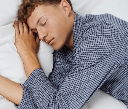Ein Mann liegt wach im Bett mit geschlossenen Augen, passend zur Frage: Warum kann ich nicht schlafen, obwohl ich müde bin?