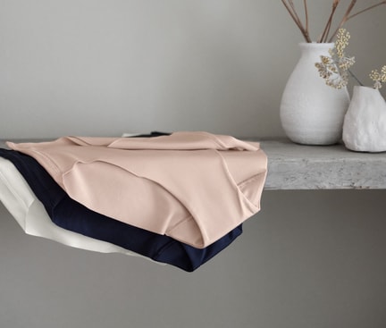Zu sehen sind drei Pantys von CALIDA aus der Serie Natural Skin in verschiedenen Farben, ordentlich auf einem Regal abgelegt.