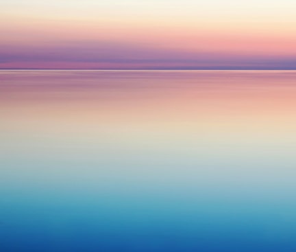 Ein beruhigender Sonnenaufgang über einem stillen Ozean, mit sanften Farbübergängen von Blau über Rosa zu hellem Gelb, die den Himmel und das Wasser harmonisch verschmelzen lassen.
