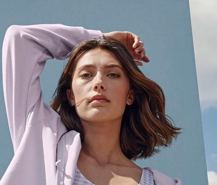 Frau mit blauem Hintergrund trägt Lavendel-Farbige Kleidung. Karierter Bustier und Loungewear-Jacke von CALIDA aus den Serien Elastic Trend und Lounge Tulip.
